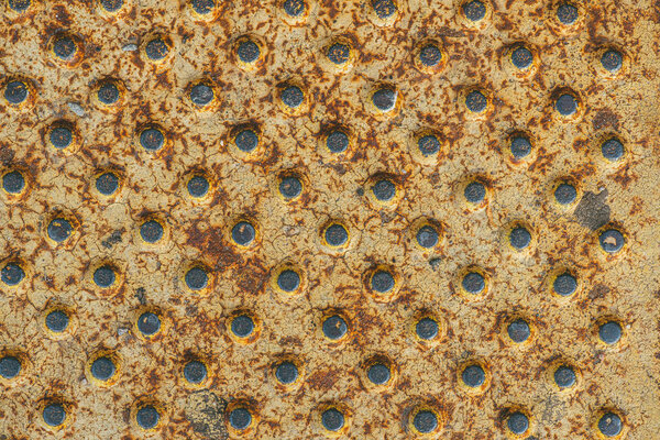 abstract metallic yellow painted rusty texture containing an array of round holes