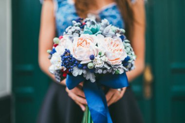 Japon polimer çamurundan yapılmış el yapımı çiçekleri tutan zarif kadın elleri. Gerçek bir düğün buketine benziyorlar. Yeşil ahşap bir kapının arkasında