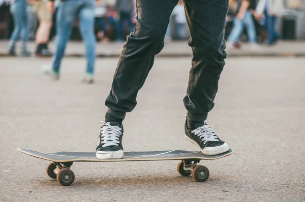 Een jongeman in donkere jeans en sneakers rijdt op een skateboard. Laag en dichtbij zicht op de voeten. Selectieve focus macro shot met ondiepe Dof — Stockfoto