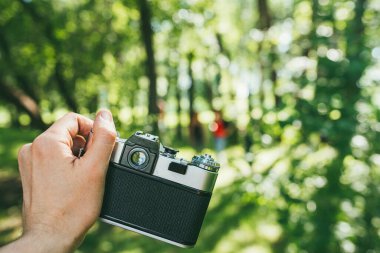 Bir adam eski bir klasik film kamerasını tutar ve yeşil bir manzaranın fotoğrafını çeker. ilk kişi görünümü Pov