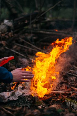 Adam ellerini ateşte ısıtıyor. Akşamları ormanda odun yakmak. Doğadaki turistik kampta kamp ateşi. Barbekü ve açık havada temiz hava. Ateş ve alev soyut karanlık arkaplanda kıvılcımlar saçar