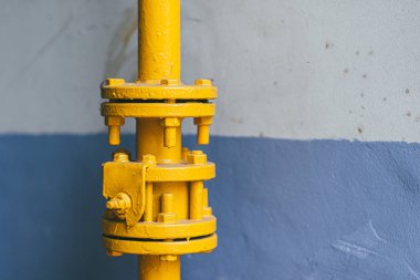 Connection of yellow gas pipes against the background of a painted blue and white wall of a residential building. Selective focus macro shot with shallow DOF