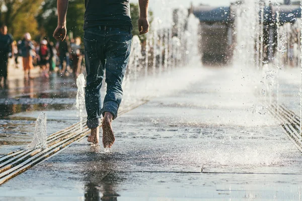 Le plan du milieu des pieds nus d'un homme en jeans qui court entre les ruisseaux de la fontaine de la ville — Photo