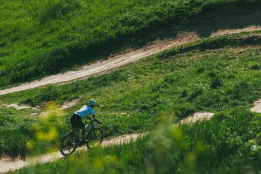 Moskova, Rusya - 21 Mayıs 2014: Dağlarda bisiklet süren genç bir kadın. Bisiklet kaskı ve üniforması var. Yokuş aşağı iniyor.