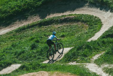 Moskova, Rusya - 21 Mayıs 2014: Dağlarda bisiklet süren genç bir kadın. Bisiklet kaskı ve üniforması var. Yokuş aşağı iniyor.