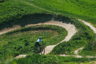 Moskova, Rusya - 21 Mayıs 2014: Dağlarda bisiklet süren genç bir kadın. Bisiklet kaskı ve üniforması var. Yokuş aşağı iniyor.