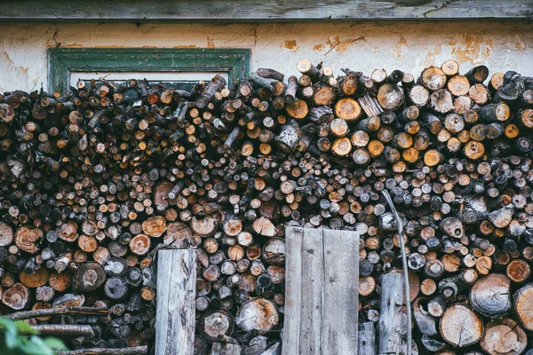 Trähög med ved på en bakgrund av ett hus vägg stänger ett grönt fönster — Stockfoto