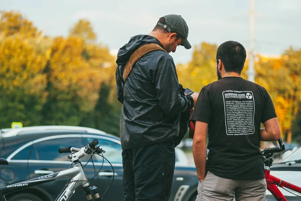 俄罗斯莫斯科- 2013年9月9日：两名骑自行车的男子站在汽车和桑尼森林的背景下互相交谈。后视镜 — 图库照片