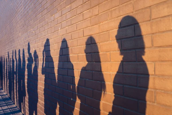 People crowd shadows lined up against a red brick wall. They are in a queue for changes in life. Social distance, covid and immigration issue concept — Stock Photo, Image
