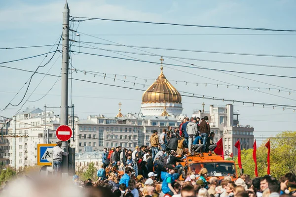 МОСКВА, Россия-9 мая 2015 г.: 9 мая в Большом Москворецком мосту люди празднуют День Победы. Люди садятся на оранжевый грузовик на заднем плане церкви Христа Спасителя. Много людей. — стоковое фото