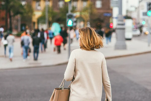 Uma jovem mulher de cabelos brancos, vestindo um casaco bege claro e carregando uma bolsa de couro, cruza uma travessia de pedestre. tiro macro foco seletivo com DOF rasa. Foto conceito de distanciamento social — Fotografia de Stock