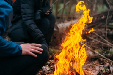 Adam ellerini ateşte ısıtıyor. Akşamları ormanda odun yakmak. Doğadaki turistik kampta kamp ateşi. Barbekü ve açık havada temiz hava. Ateş ve alev soyut karanlık arkaplanda kıvılcımlar saçar