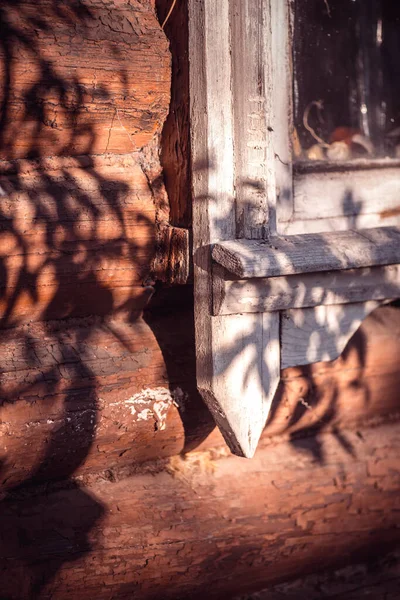 Время от времени старое белое окрашенное деревянное окно с отшелушивающей краской на деревянном бревенчатом фасаде, освещенном ярким солнцем, отбрасывающим тень от дерева. Выборочный фокус макросъемки с неглубокой глубиной резкости — стоковое фото