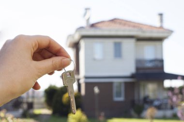 Evin anahtarlarını yeni bir evin önünde, ev şeklindeki anahtarlıkta tutmak.