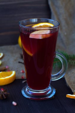 Bir bardak portakal, elma ve baharat dilimli sıcak şarap, tarçın ve anason yıldızı ahşap bir masada kış süslemeleri ile. Dikey. Kışın ve sonbaharın sıcak içecekleri. 