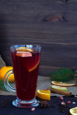 Bir bardak portakal, elma ve baharat dilimli sıcak şarap, tarçın ve anason yıldızı ahşap bir arka planda kış süslemeleri ile. Kışın ve sonbaharın sıcak içecekleri. dikey