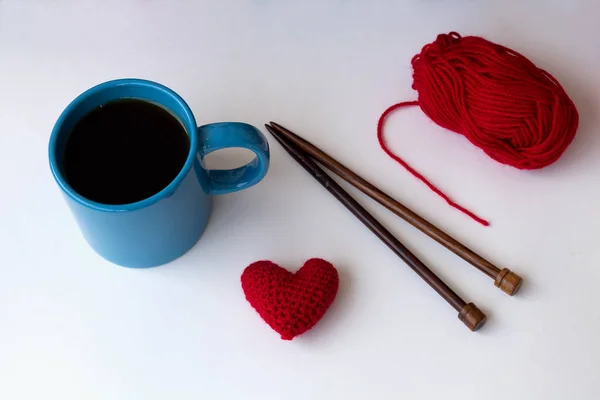 cup of black coffee and red heart of yarn with red ball of yarn with needles on white background top view