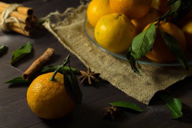 Taze turuncu mandalinalar ve ahşap zemin üzerinde cam bir tabakta yeşil yapraklar. Karanlık bir masada olgun meyveler. Dikkat çekmeden. yatay