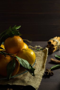 Masanın üzerinde olgun meyveler var. Taze turuncu mandalinalar ve koyu ahşap zemin üzerinde cam bir tabakta yeşil yapraklar. Dikkat çekmeden. dikey