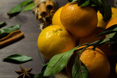 Ahşap arka planda yeşil yapraklı taze turuncu mandalinalar. Dikkat çekmeden. Olgun meyveler karanlık masada tarçın ve baharatlarla.