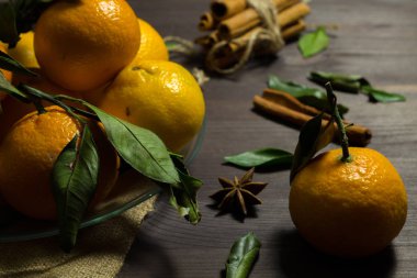 Tahta masadaki taze mandalinalar. Ahşap arka planda yeşil yapraklı taze turuncu mandalinalar. Dikkat çekmeden. Olgun meyveler karanlık masada tarçın ve baharatlarla.