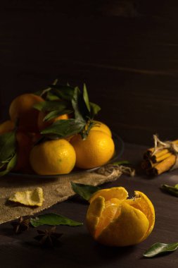 Dikkat çekmeden. Ahşap arka planda yeşil yapraklı taze turuncu mandalinalar. Olgun meyveler karanlık masada tarçın ve baharatlarla.
