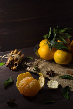 Ahşap masada olgun bir mandalina. Taze turuncu mandalinalar ve cam bir plaka içinde yeşil yapraklar. Koyu ahşap arka planda baharatlı. alçak tuş.