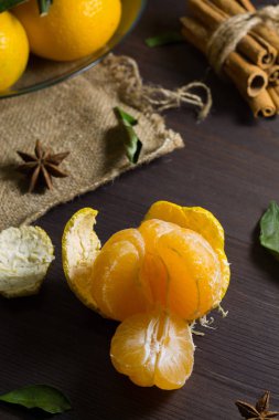 Ahşap masada soyulmuş mandalina. Taze ve olgun portakal mandalinaları. Koyu ahşap arka planda, yeşil yapraklar ve baharatlar. Dikkat çekmeden. dikey