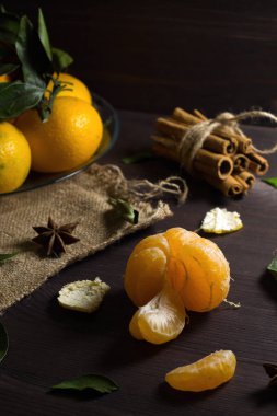 Ahşap masada soyulmuş mandalina. Dikkat çekmeden. Ahşap arka planda yeşil yapraklı taze turuncu mandalinalar. Olgun meyveler karanlık masada tarçın ve baharatlarla.