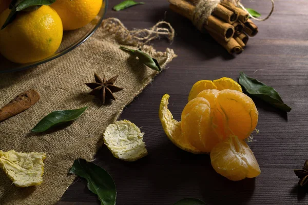 Ahşap masada soyulmuş mandalina. Taze ve olgun portakal mandalinaları. Koyu ahşap arka planda, yeşil yapraklar ve baharatlar. alçak tuş.