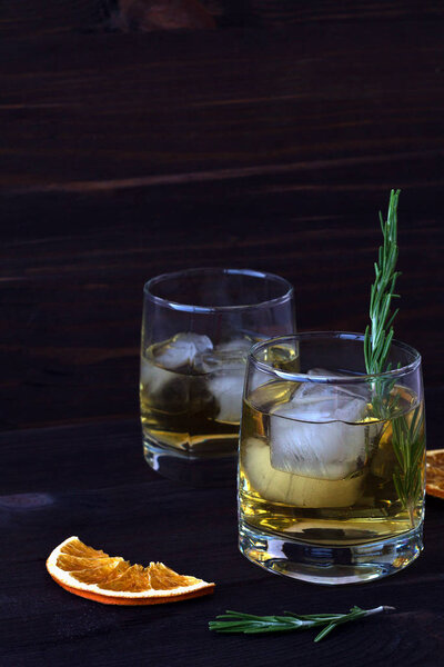 lemonade in a two glasses with pieces of ice and a sprig of rosemary on a dark background. glass of whiskey or cocktail with ice with slices of orange on a wooden table. 