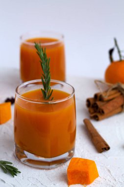 Bir bardak taze balkabağı suyu ve portakallı olgun kabak dilimleri ve beyaz arka planda baharatlar. Biberiye filizi ve mandallı tarçınlı taze meyve suyu..