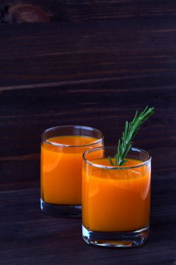 Detoks kokteyli. iki bardak taze balkabağı suyu, havuç ya da portakal, koyu ahşap arka planda biberiye filizi. düşey yönelim.