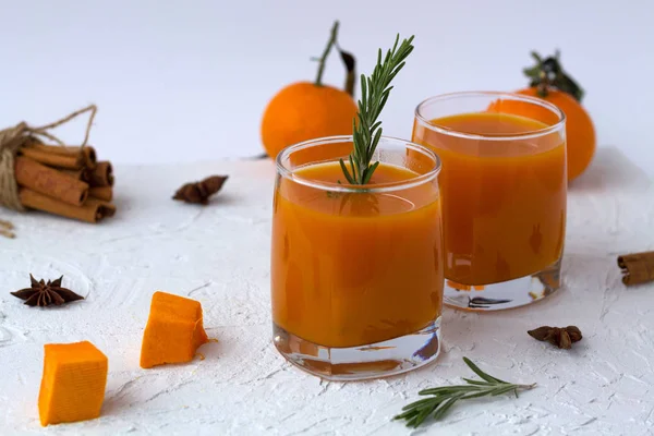 fresh cocktail with sprig of rosemary and sticks of cinnamon with mandarins on white table. two glasses of fresh pumpkin juice and oranges with slices of ripe pumpkin and spices on a white background.