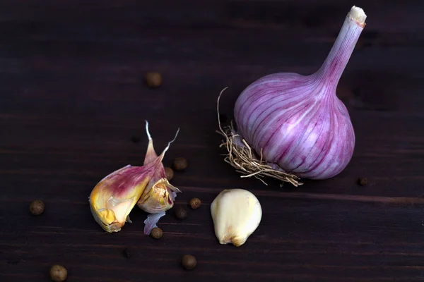 fresh garlic and black pepper. unpeeled cloves of fresh garlic on a dark table. healthy and wholesome food. fresh garlic and on a wooden background. horizontal orientation.