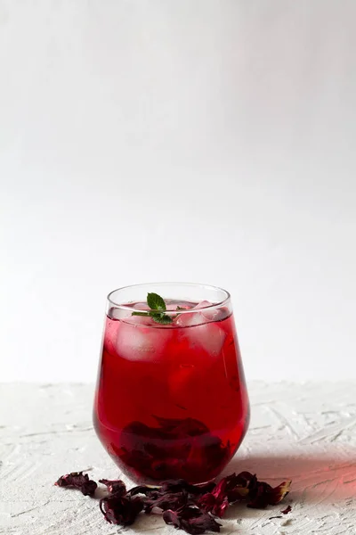 Szklanka Mrożonej Czerwonej Herbaty Hibiskusa Suchymi Kwiatami Róż Białym Stole — Zdjęcie stockowe
