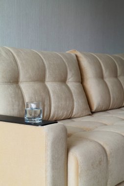 Koltuğun kolunda bir bardak su. Oturma odasındaki kahverengi kanepenin detayları. Biraz ara ver..
