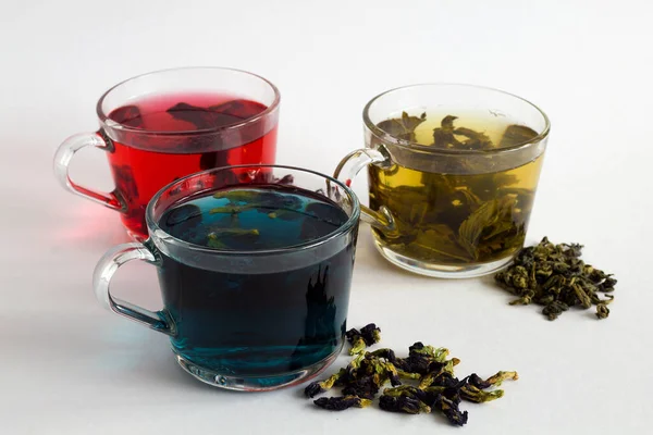 butterflu pea tea. Blue herbal hot tea. Three glass cups with blue, red and green tea with dry tea leaves and flowers on a white background. Red hot Hibiscus tea. Green hot tea. Hot drinks. Healthy lifestyle.