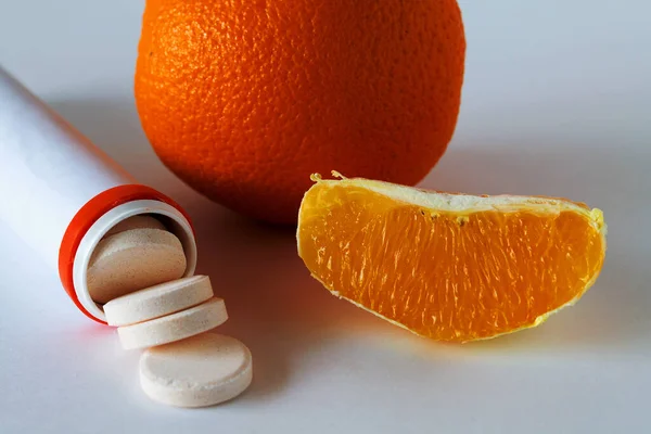 vitamin C pills isolated on white background, fresh slice of orange on white table. orange pill bottle with pills. to strengthen the immune system. Healthy lifestyle. citrus fruit
