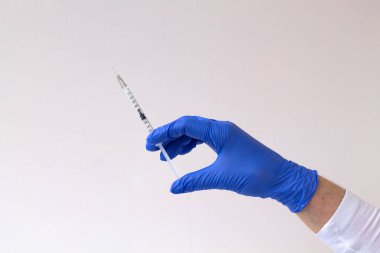 Sağlık sigortası. Gri arka planda bir şırınga tutan eldivenli el. Mavi eldivenli doktor elinde şırınga tutuyor. Laboratuvardaki beyaz üniformalı insanlar. Boşluğu kopyala.