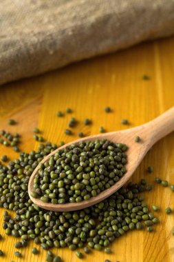 Kurumuş fasulyeli ahşap kaşık ve ahşap bir masada çuval bezi. Sağlıklı bir yaşam tarzı. Sarı arka planda çuval beziyle kaşıkta yeşil fasulye. kopyalama alanı. dikey