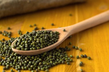 Sarı arka planda çuval beziyle kaşıkta yeşil fasulye. Kurumuş fasulyeli ahşap kaşık ve ahşap bir masada çuval bezi. kopyalama alanı. Sağlıklı yaşam tarzı.