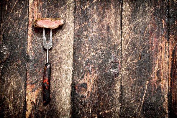 Grelha de carne. Um pedaço de porco grelhado num garfo. Na velha mesa de madeira . — Fotografia de Stock