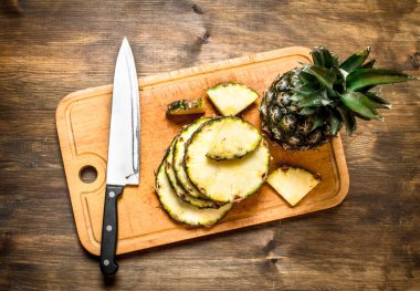 Bir bıçak ile kesme tahtası üzerinde ananas dilimlenmiş.