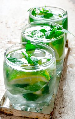 Üç kokteyl bardağı buz, kireç, nane yaprakları ve ROM ile. Eski arka plan üzerinde.