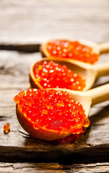 Caviar rojo en una cuchara de madera. Sobre fondo de madera . — Foto de Stock