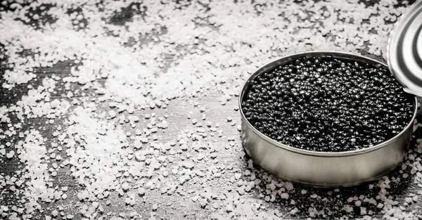 Caviar negro en un frasco con sal. Sobre mesa de madera negra . — Foto de Stock
