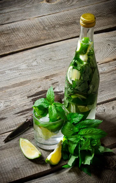 Cocktail in vetro e bottiglia, anche menta e lime su un tavolo di legno  . — Foto Stock