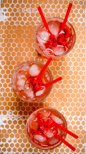 Three red cocktail with ice and straws .