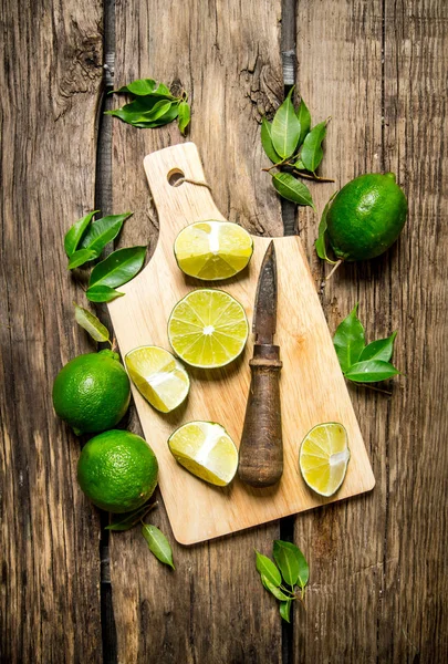 Limes affettato su una tavola di legno con foglie e coltello . — Foto Stock